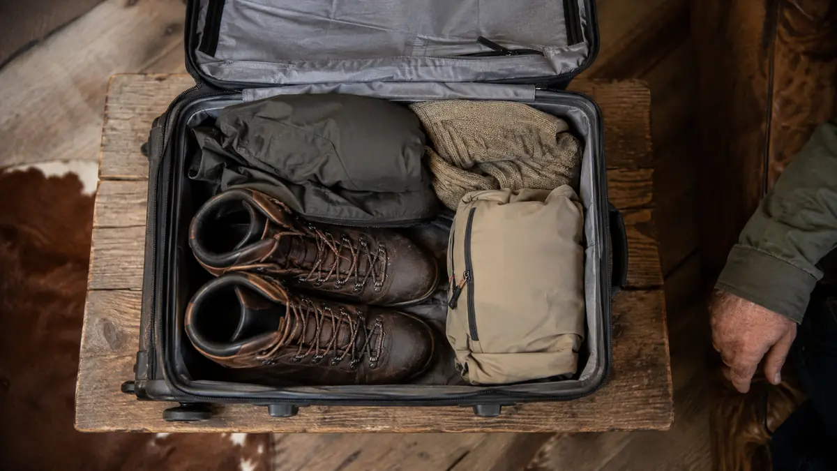 Packable daypack folded flat and tucked inside a carry-on suitcase next to boots and a jacket