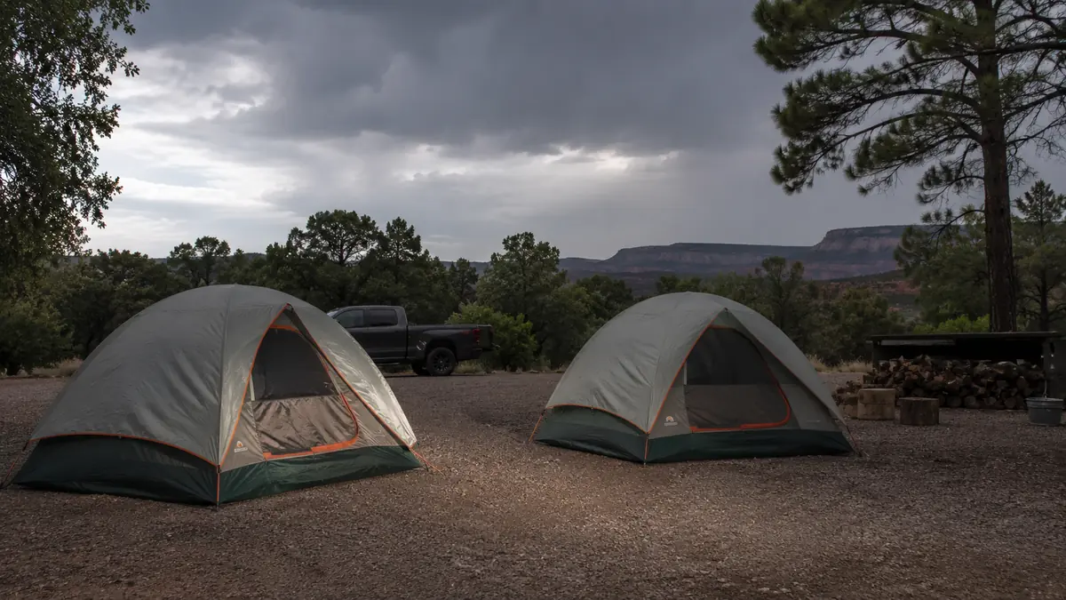 Two dome tents pitched side by side on a gravel campsite under a gray, threatening sky