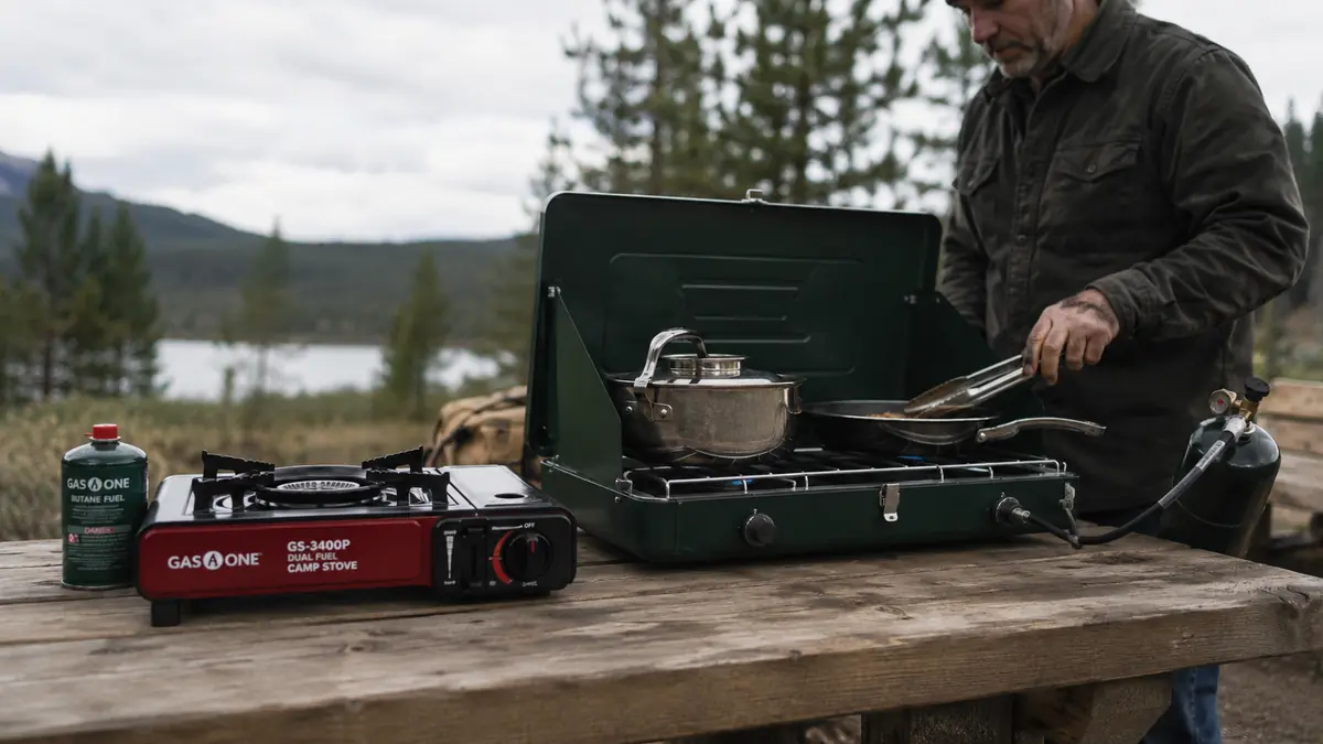 Gas One GS-3400P and a two-burner Coleman propane stove set up side by side on a picnic table