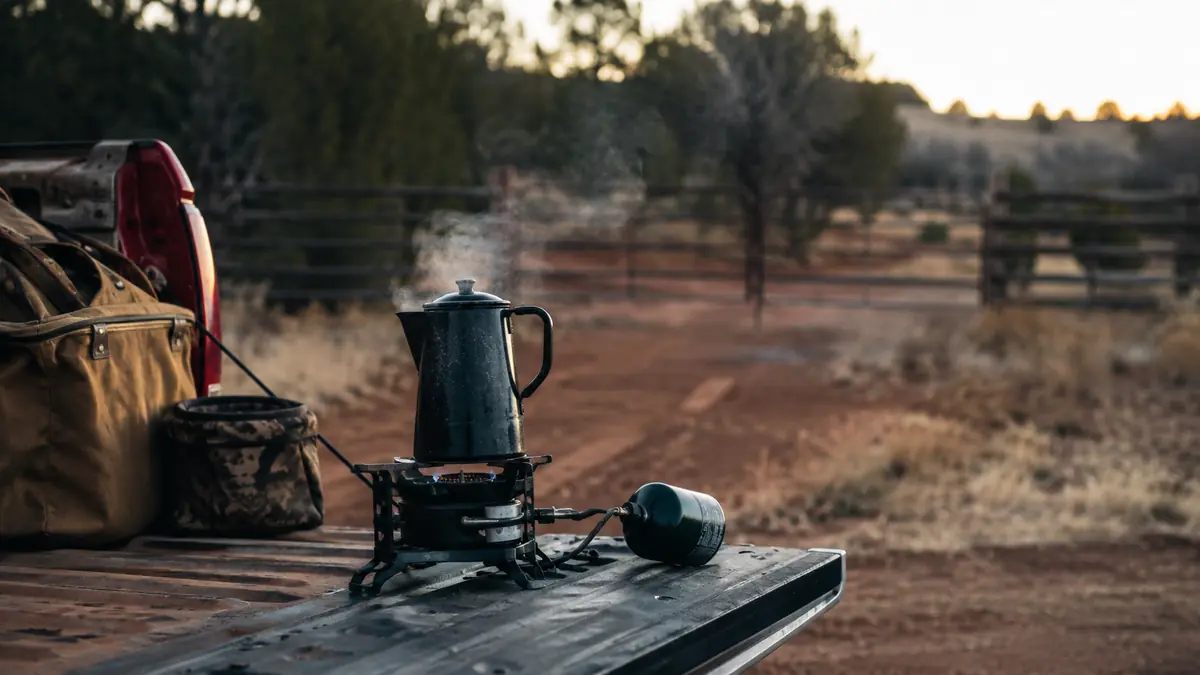 Gas One GS-3400P dual fuel camp stove set up on a tailgate with a coffee pot heating at sunrise