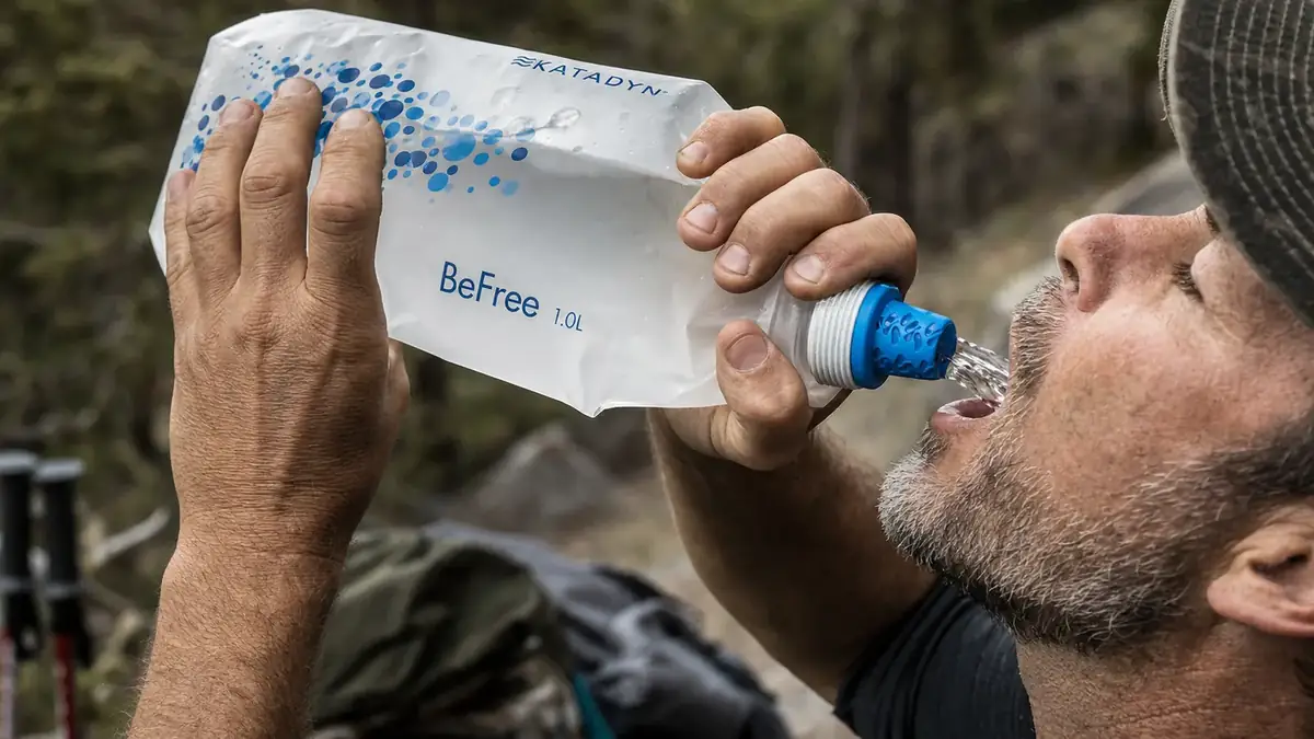 Close view of hands squeezing a collapsible flask through a filter cap into a mouth