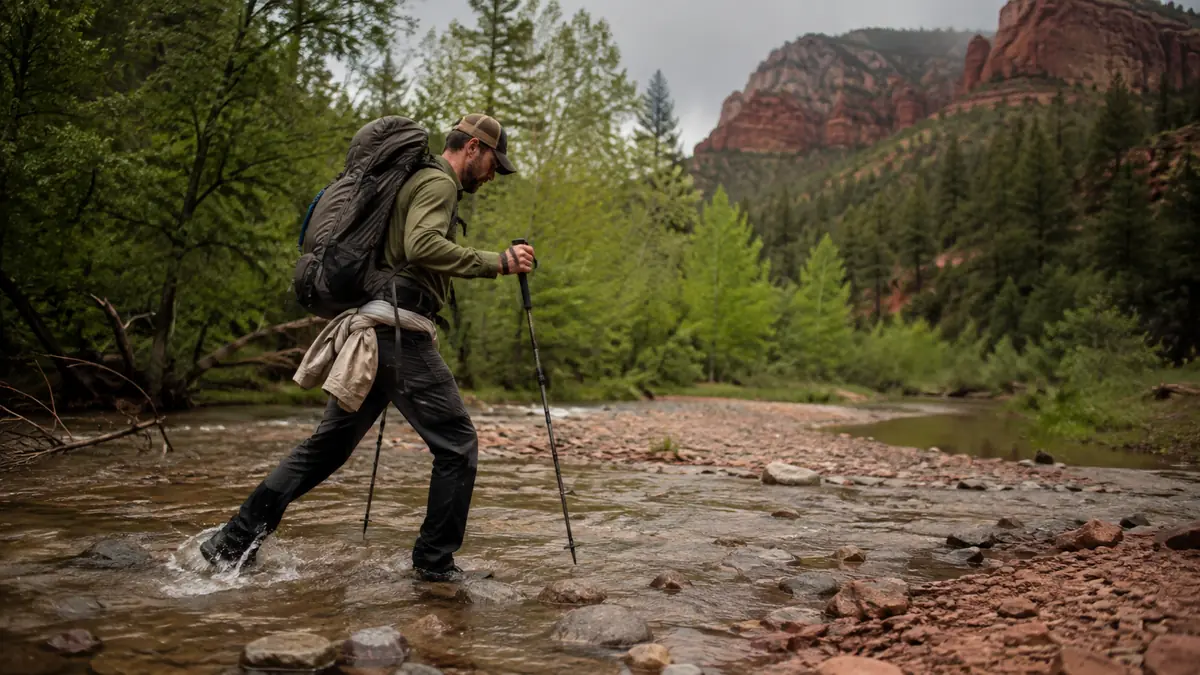 Hiker crossing a shallow rocky creek using trekking poles for balance
