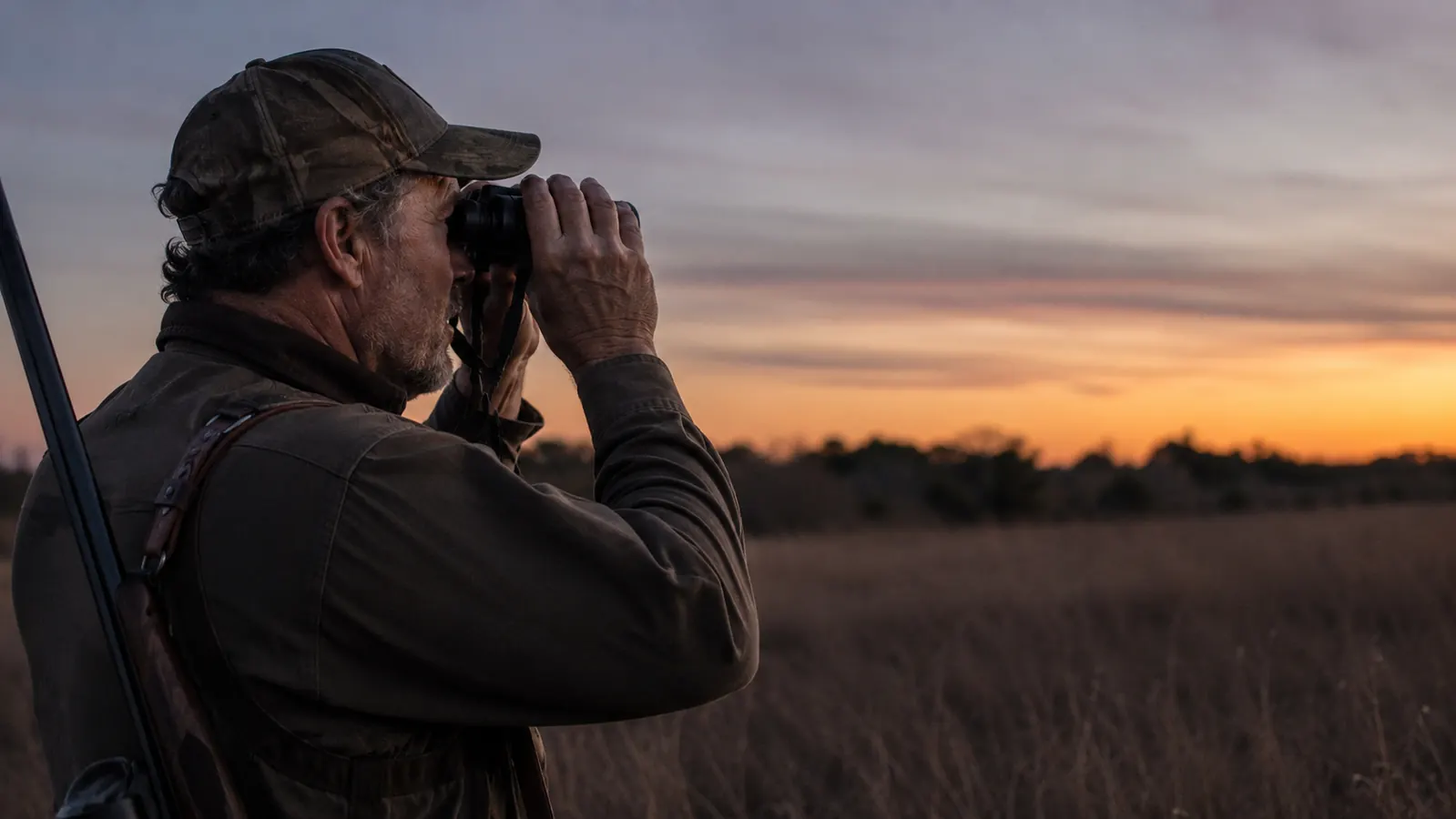 Hunter glassing a low-light tree line at dusk with binoculars raised